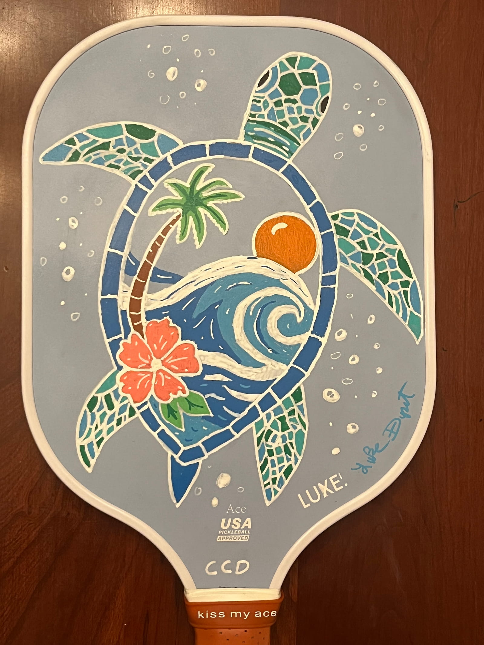 Hand-painted pickleball paddle with a mosaic-style sea turtle framing a wave, palm, and hibiscus
